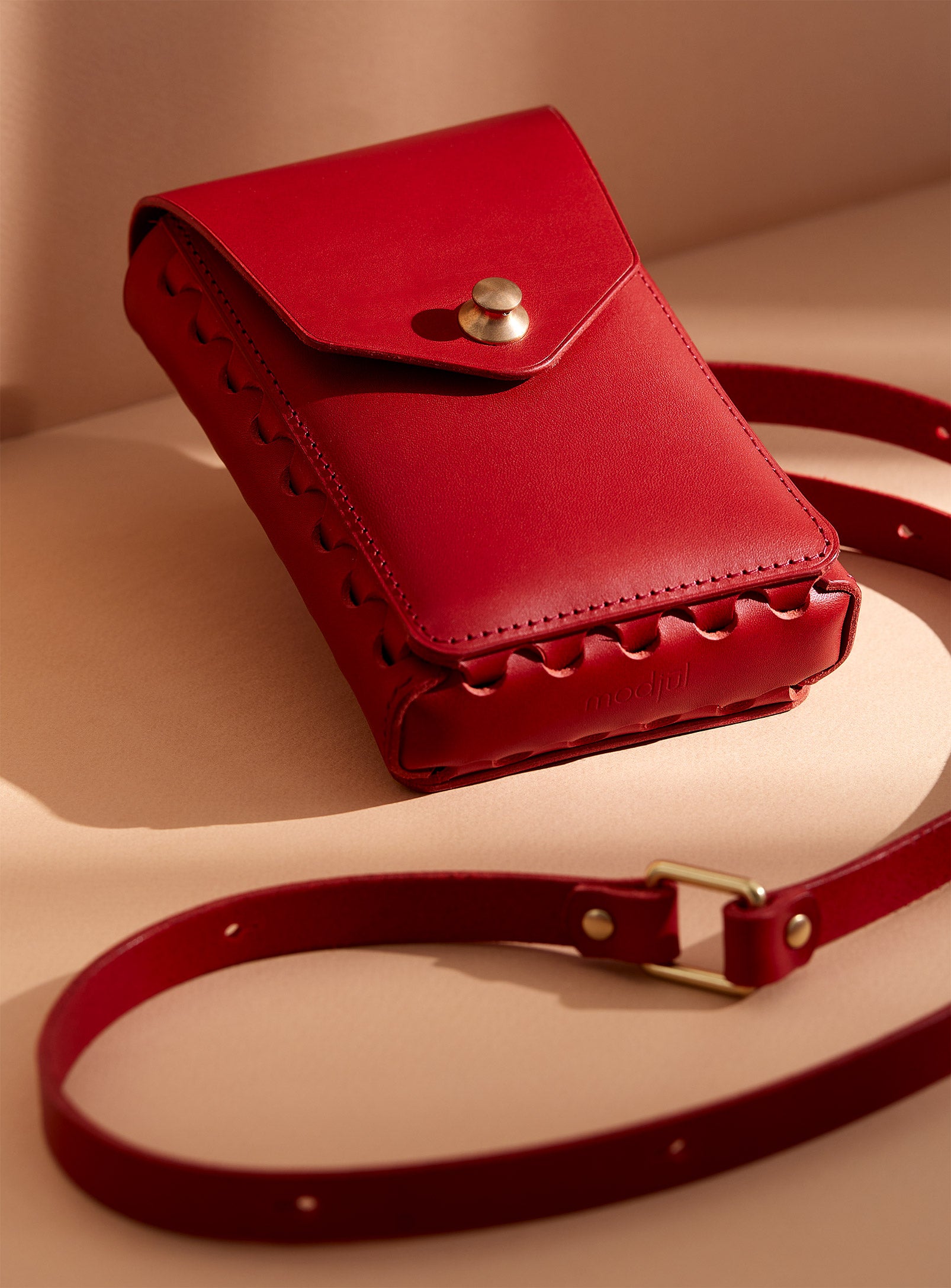 modjūl's capsule leather bag in red. A rectangular-shaped bag with long straps, perfect for a phone.