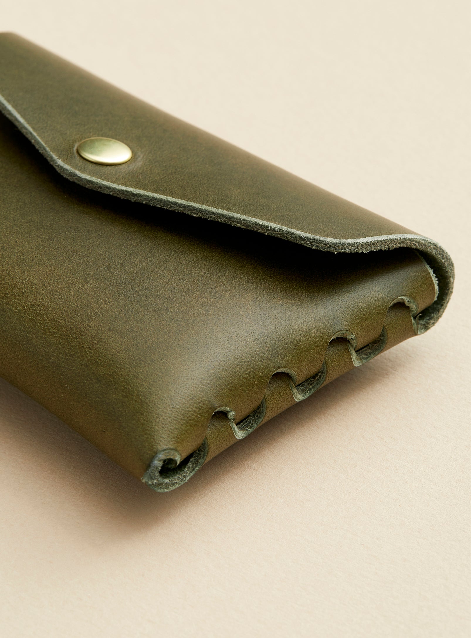 The side profile of modjūl's classic pouch in olive colored leather. A compact open wallet with endless possibilities, perfect for holding cards, keys or loose change. Handmade in Canada and joined with the signature modjūl joinery and quality brass hardware.