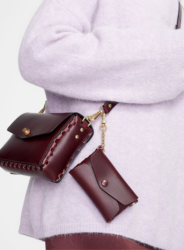 Someone wearing the modjūl leather crossbody bag and leather chain pouch in burgundy, made in Canada.