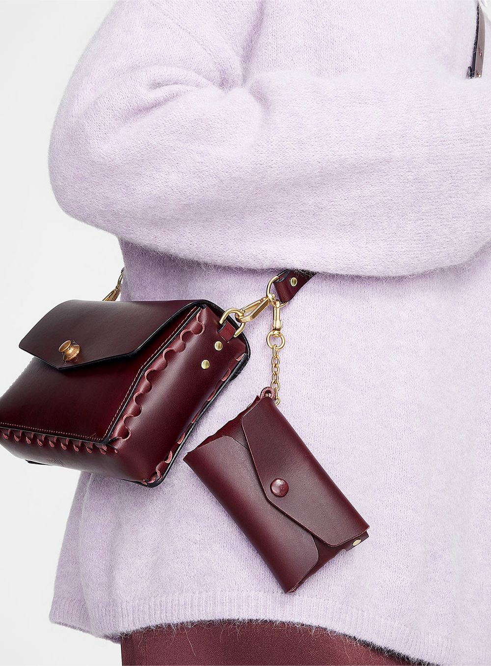 Someone wearing modjūl's petite crossbody leather bag with the leather chain pouch attached. Both in burgundy and made in Canada.