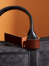 The modjūl leather traveller’s tag in brown, displayed on a duffle bag. A luggage tag constructed using quality vegetable-dyed Italian leather with the option for personalization.