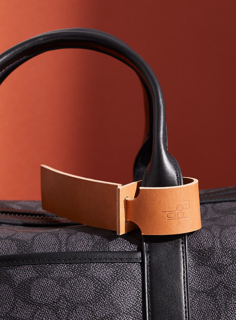 The modjūl leather traveller’s tag in camel, displayed on a duffle bag. A luggage tag constructed using quality vegetable-dyed Italian leather with the option for personalization.