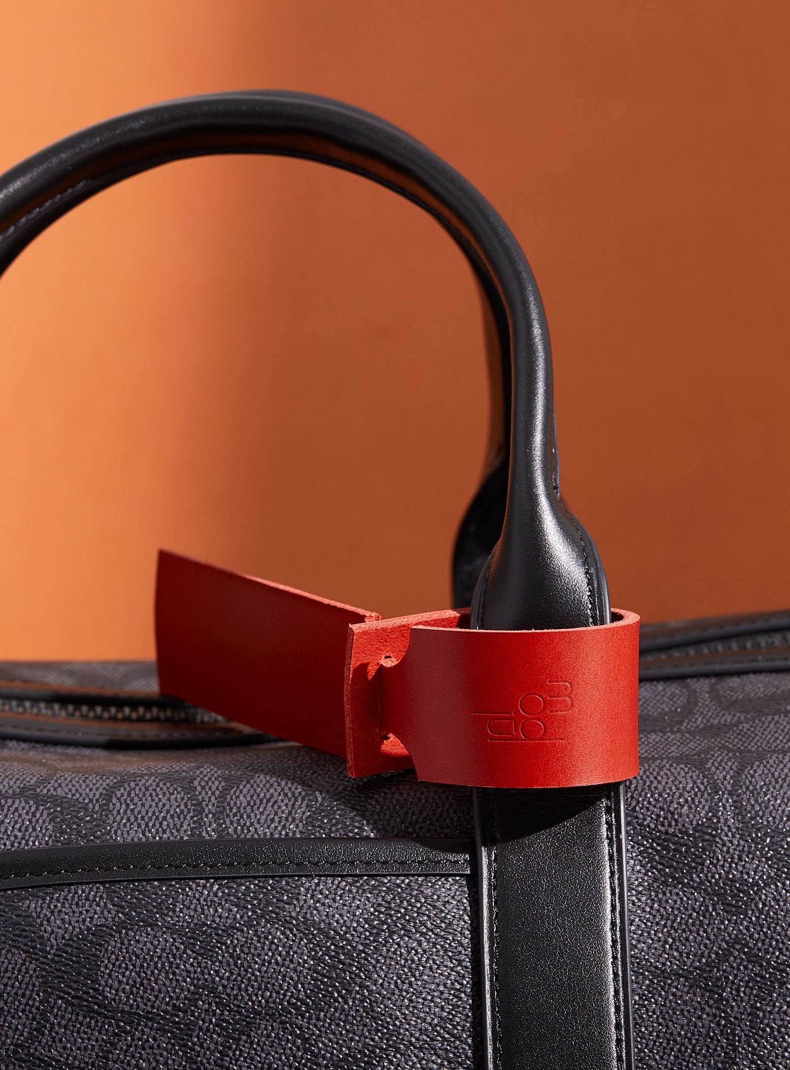 The modjūl leather traveller’s tag in red, displayed on a duffle bag. A luggage tag constructed using quality vegetable-dyed Italian leather with the option for personalization.