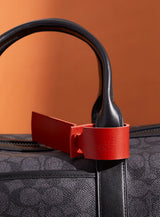 The modjūl leather traveller’s tag in red, displayed on a duffle bag. A luggage tag constructed using quality vegetable-dyed Italian leather with the option for personalization.