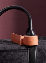 The modjūl leather traveller’s tag in pink, displayed on a duffle bag. A luggage tag constructed using quality vegetable-dyed Italian leather with the option for personalization.