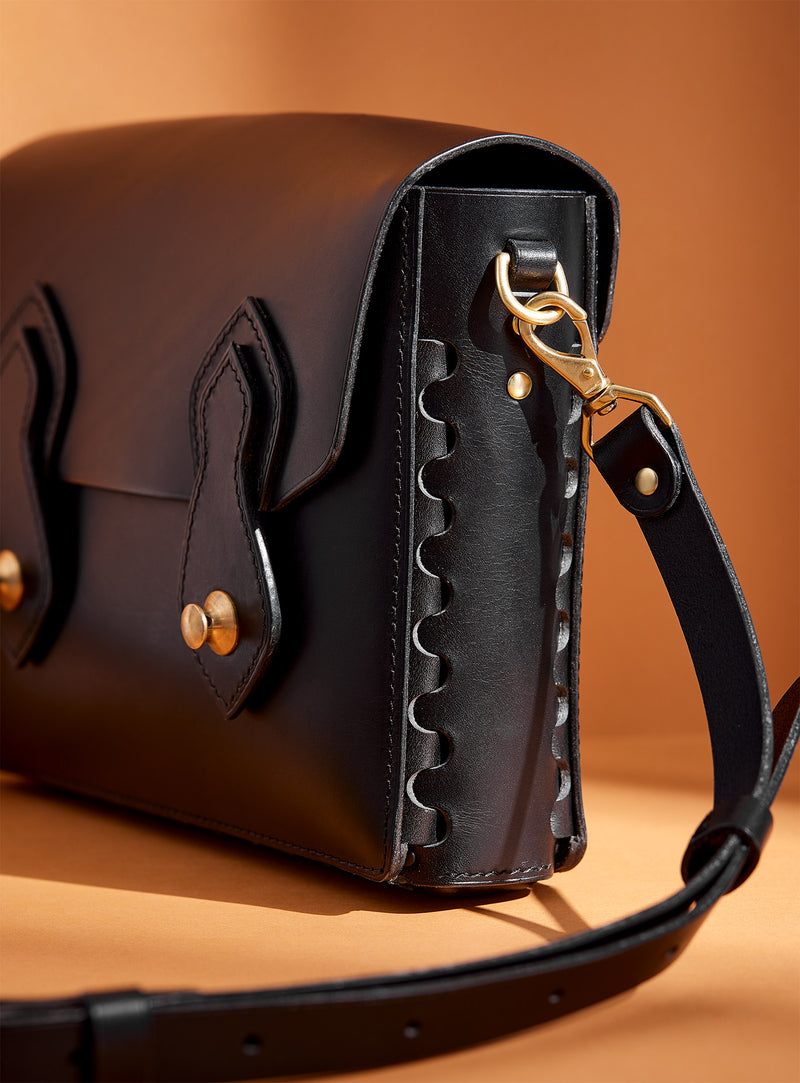 The side profile of the Odyssey bag in black vegetable dyed Italian leather, showcasing modjūl's signature joinery and premium brass hardware. Experience the feeling of quality.