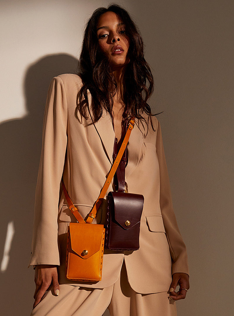 A woman in a suit wearing two modjūl capsule bags around her neck. One crafted using yellow leather, the other constructed using burgundy leather. 
