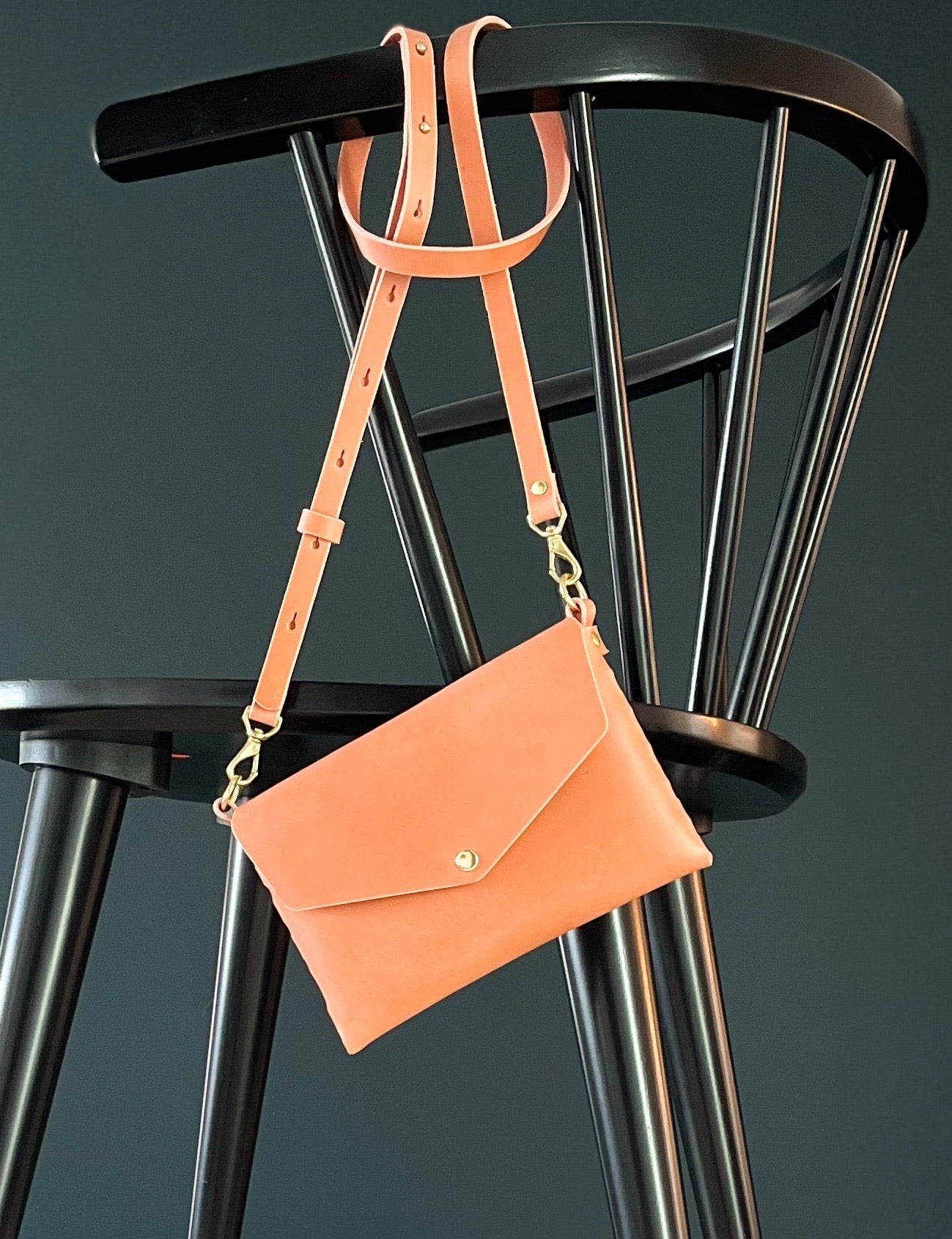modjūl's mini leather bag in pink hanging on the back of a chair. A rectangular-shaped bag with long straps, handmade in Canada using quality Italian leather and brass hardware.