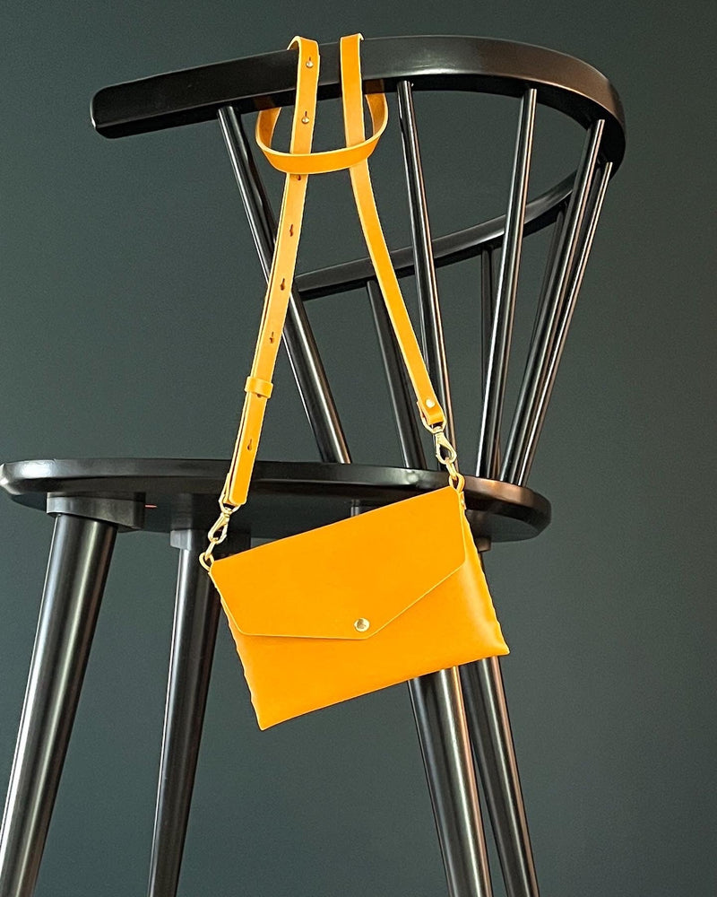 modjūl's mini leather bag in yellow hanging on the back of a chair. A rectangular-shaped bag with long straps, handmade in Canada using quality Italian leather and brass hardware.
